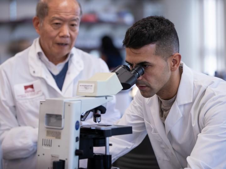 Student and professor examine microscope in lab